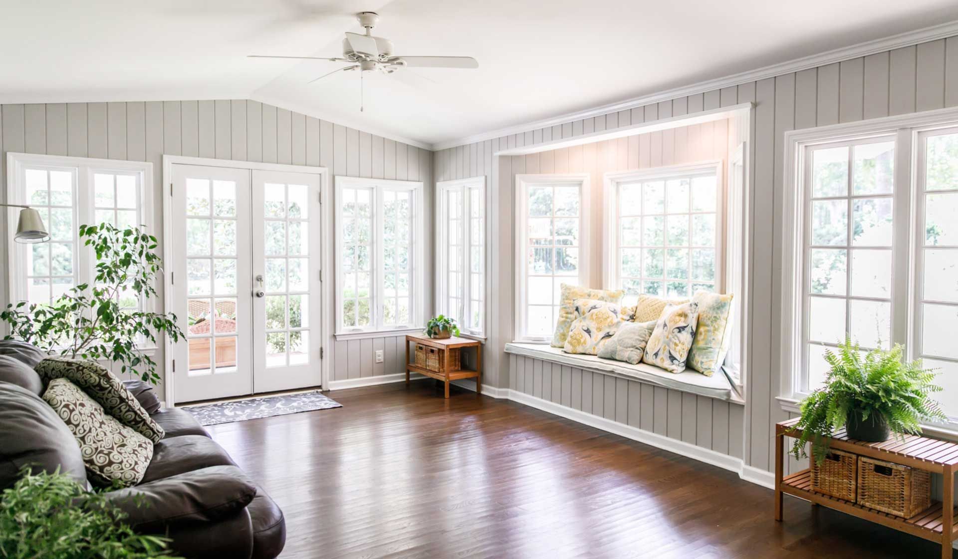 Bright living room with dark wood floors, gray paneling, and a window seat with pillows.