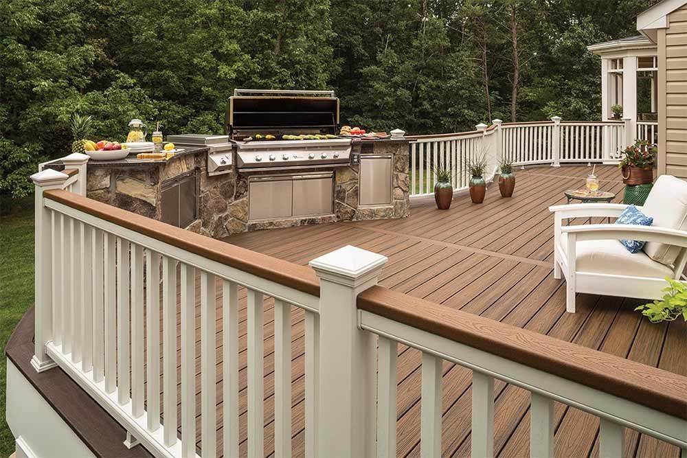 Outdoor deck with built-in grill and counter. White railings, composite decking, and greenery in the background.