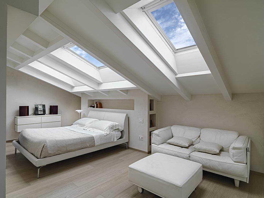 White bedroom with skylights, bed, couch, and ottoman.