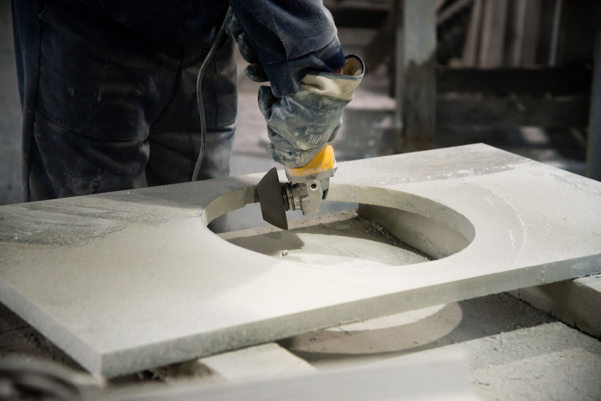 Person using a power tool to cut a circular hole in a stone countertop in a workshop.