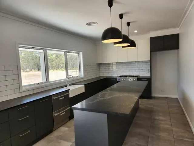 An Empty Kitchen With Black Cabinets and a Large Island — Evoke Building Group In Daylesford, VIC
