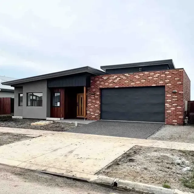 Modern house with brick and gray facade, garage, and driveway under an overcast sky.