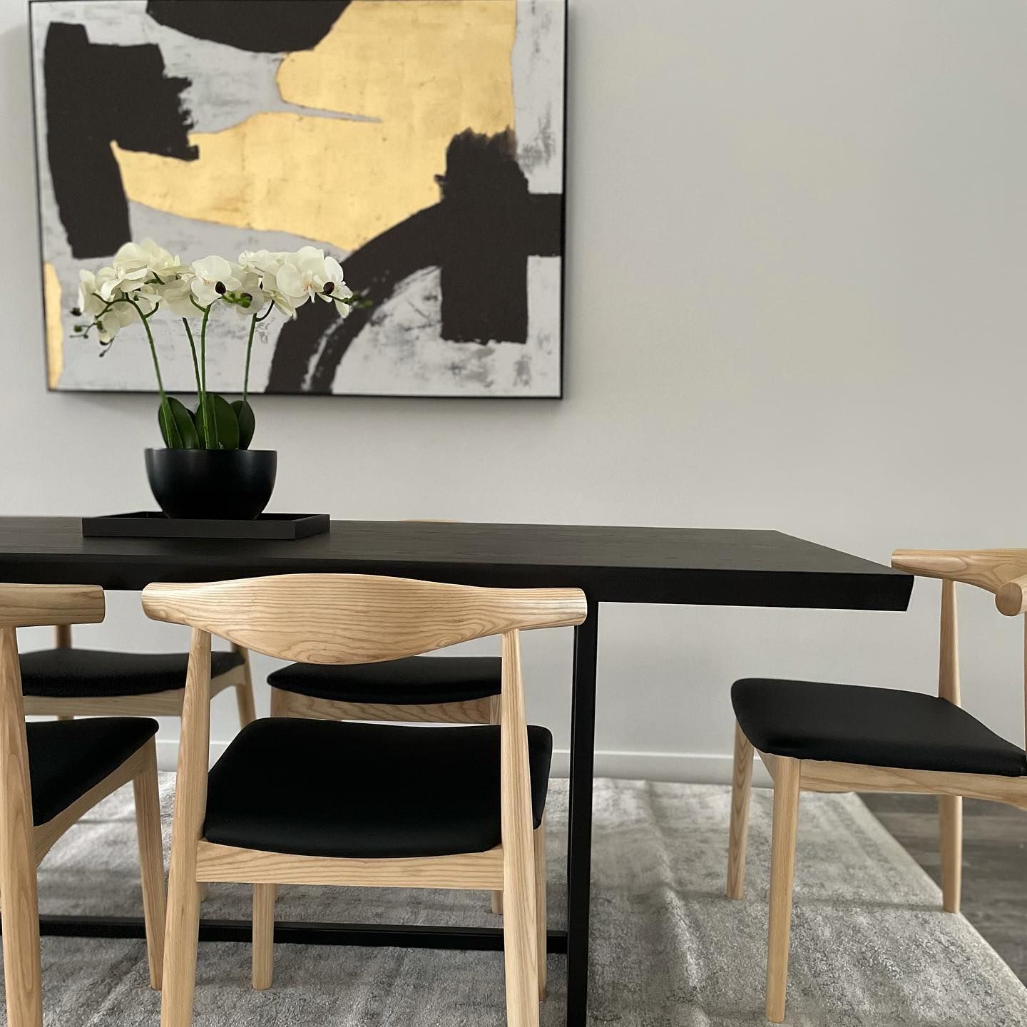 Dining room with black table, wooden chairs, abstract art, and white flowers.