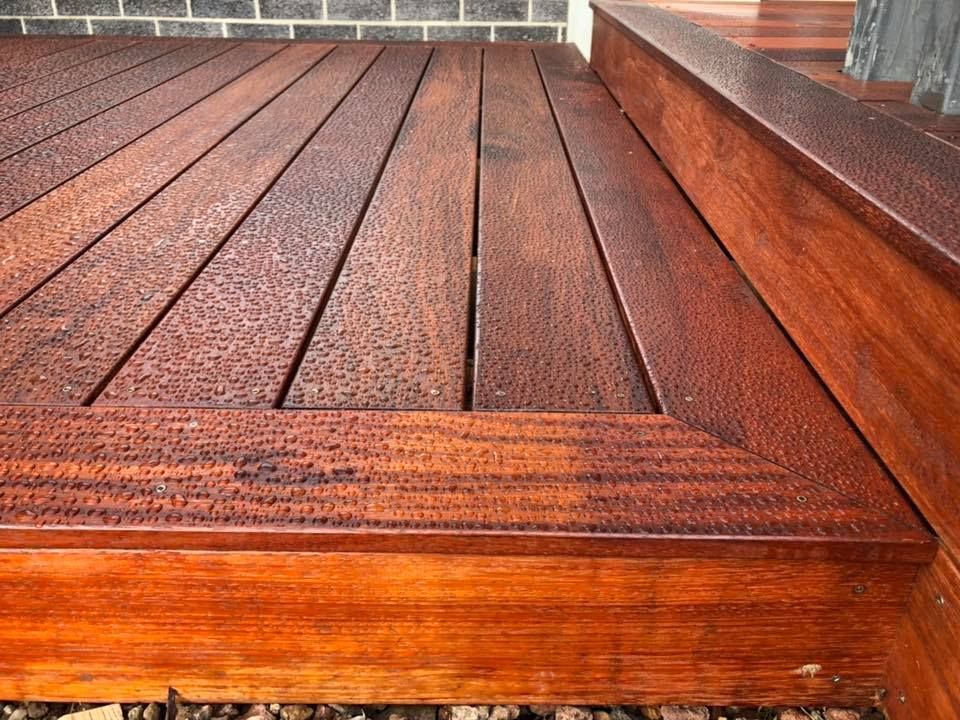 Close-up of a wet, reddish-brown wooden deck with a border and grooves.