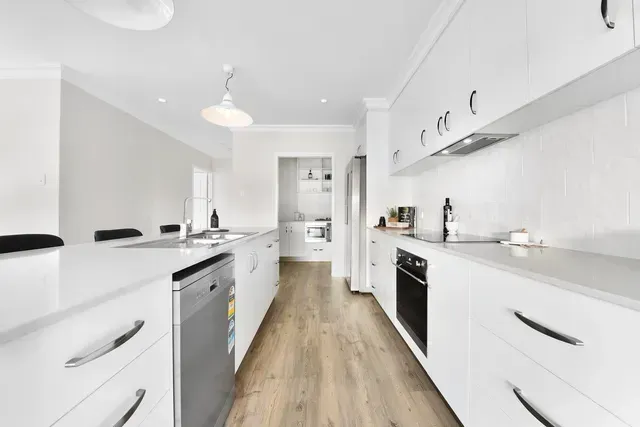 A Long Kitchen With White Cabinets and Wooden Floors — Evoke Building Group In Ballarat Central, VIC