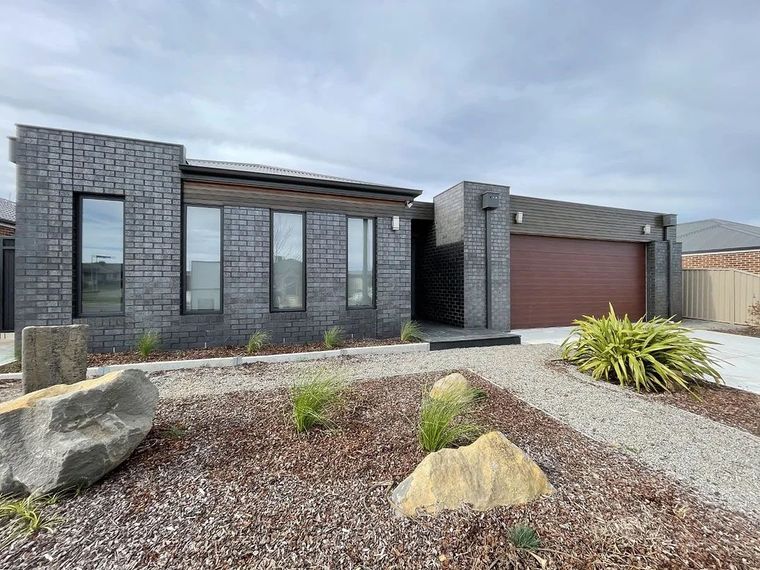 Modern house with dark brick facade, three tall windows, brown garage door, and a rock garden.