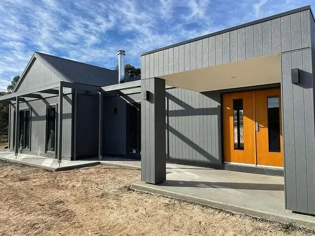 A Gray House With Orange Doors is Sitting on Top of a Dirt Field — Evoke Building Group In Ballarat Central, VIC