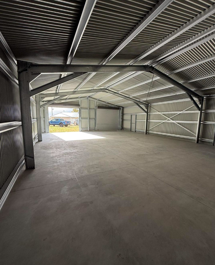 Empty metal warehouse interior with open doors, concrete floor, and steel beams.