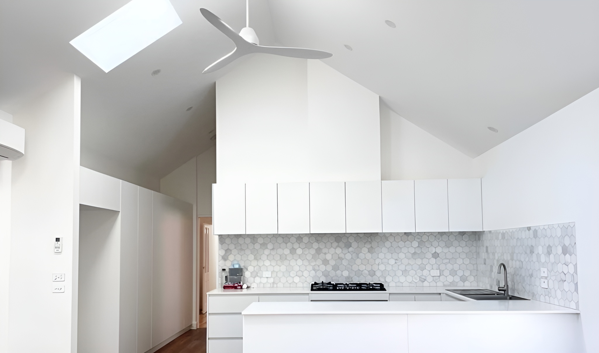 Modern white kitchen with vaulted ceiling, skylight, and white cabinets.
