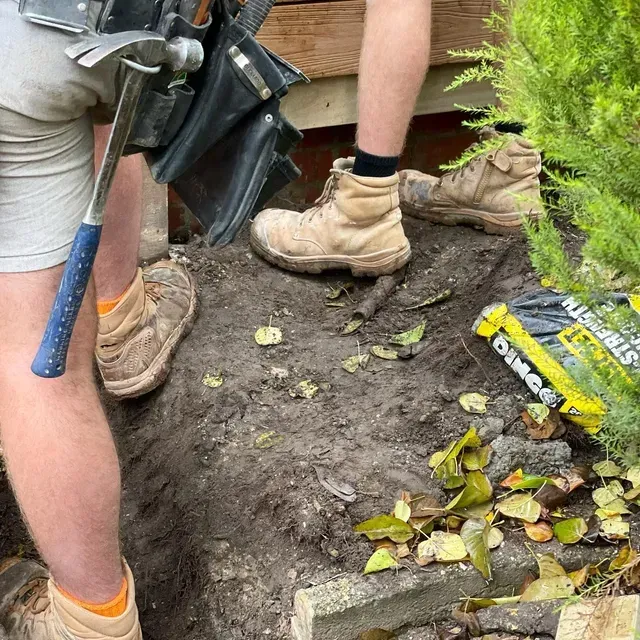 A Man is Digging in the Dirt With a Hammer and Shovel — Evoke Building Group In Ballarat Central, VIC