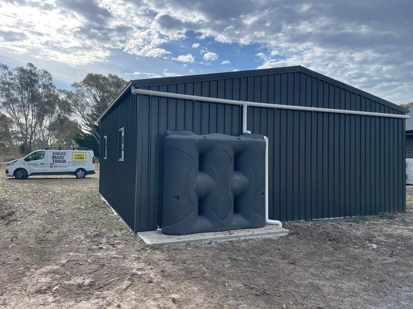 Dark shed with rainwater tank and white van in yard.