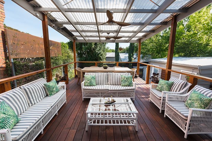Outdoor deck with white wicker furniture, green and white striped cushions, and a clear roof.