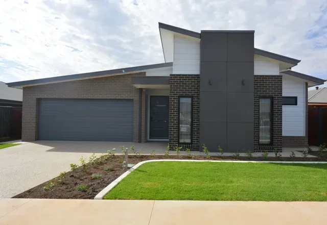 A Modern House With a Large Garage and a Lush Green Lawn in Front of It — Evoke Building Group In Ballarat Central, VIC