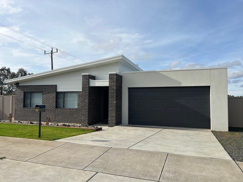 Modern house with dark garage door, brick facade, and white trim under a cloudy sky.