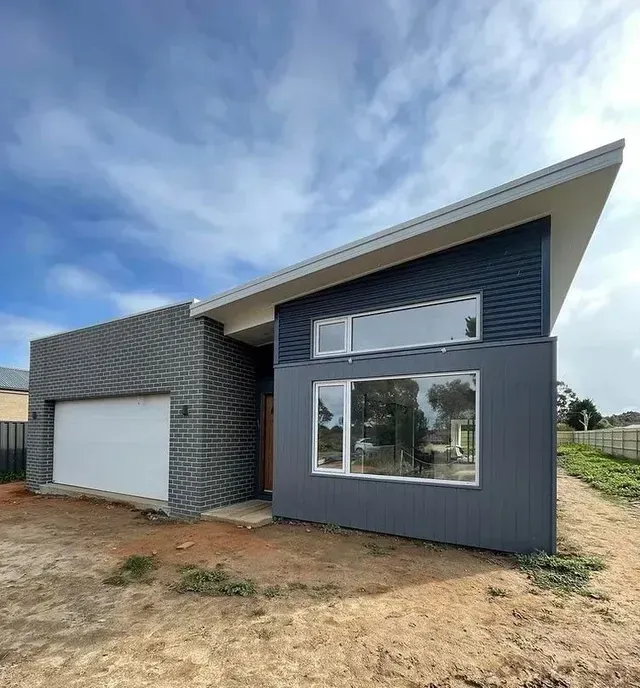 A House With a Garage and a Large Window is Sitting on Top of a Dirt Field — Evoke Building Group In Ballarat Central, VIC