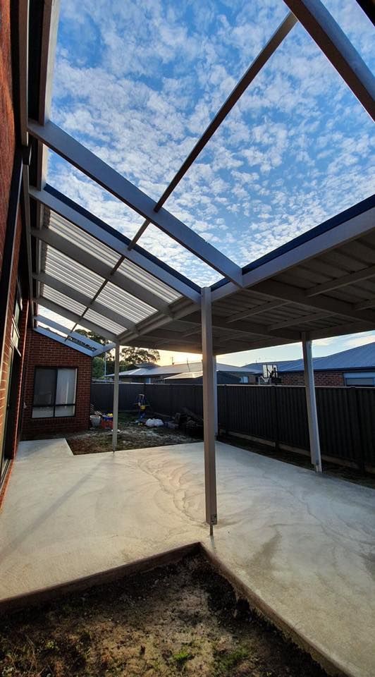 Patio with corrugated roof extending from brick building, blue sky visible.