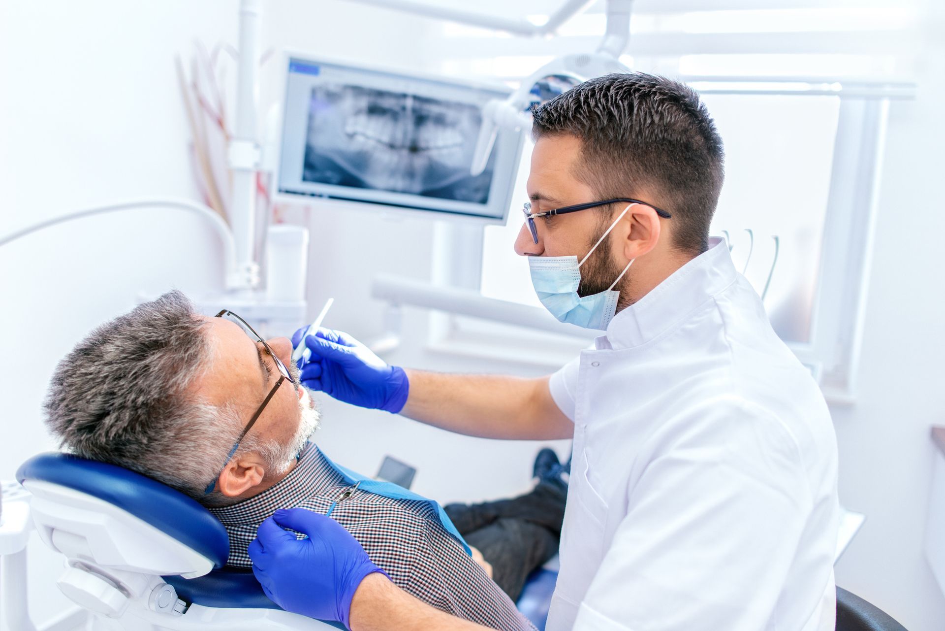 A man sits in a dental chair while a periodontist inspects his teeth for health issues.