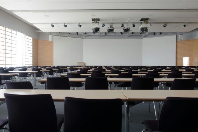 Empty conference room with rows of tables and chairs facing a blank screen and podium.