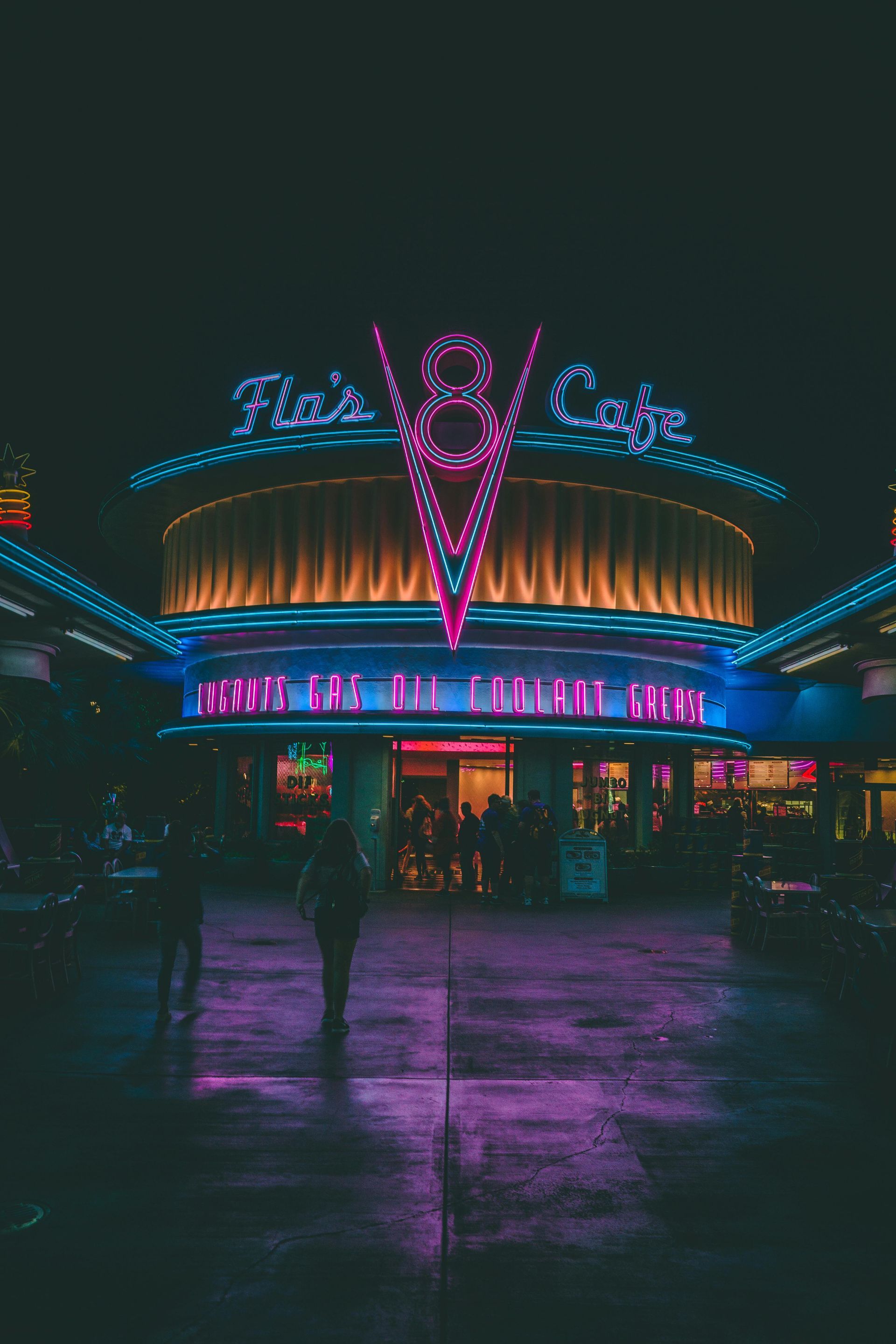 Flo's V8 Cafe at night, glowing neon sign. People walk in front of the illuminated restaurant.