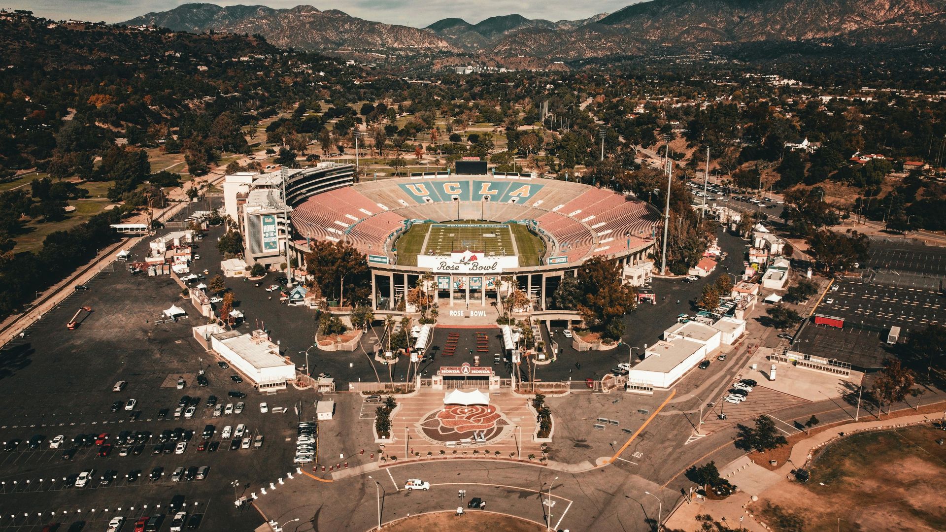 Aerial view of the Rose Bowl stadium in Pasadena, California. Green football field, parking, and surrounding hills.