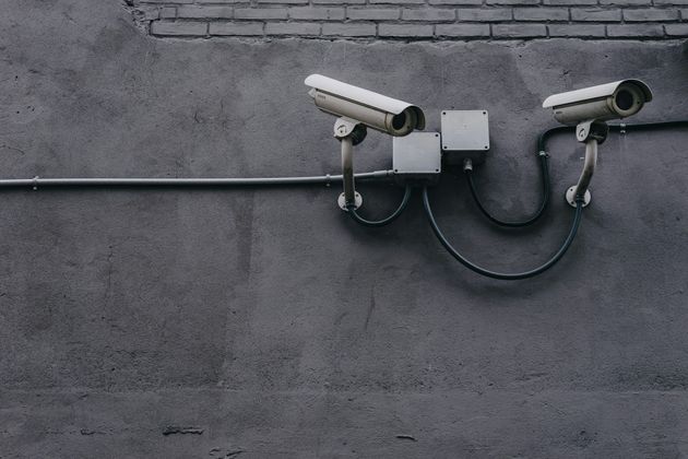 Two security cameras mounted on a gray concrete wall, near an electrical box and brick section.