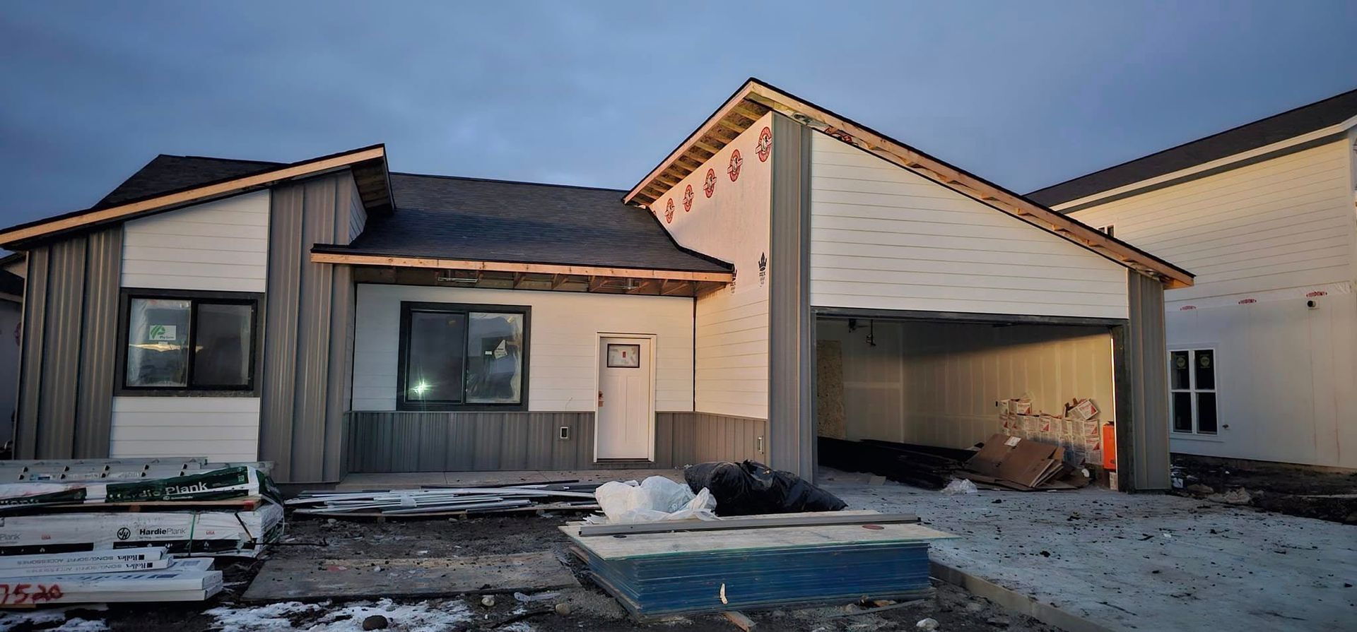 A newly constructed single-story house with gray board-and-batten siding, white accents, and an open garage.