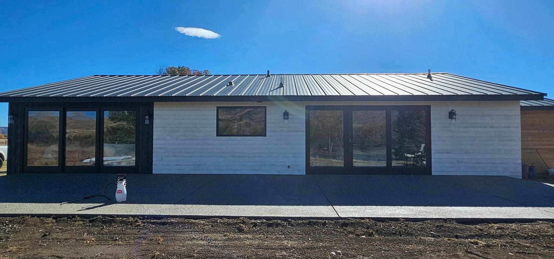 Modern single-story home with a metal roof, white horizontal siding, and two sets of large glass doors under a blue sky.