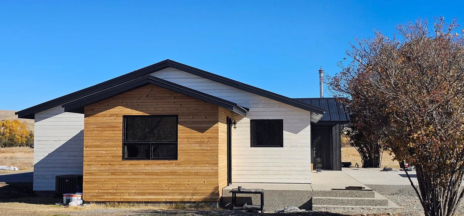 A single-story house with a white horizontal siding, a light wood-paneled accent section, and a black peaked roof.