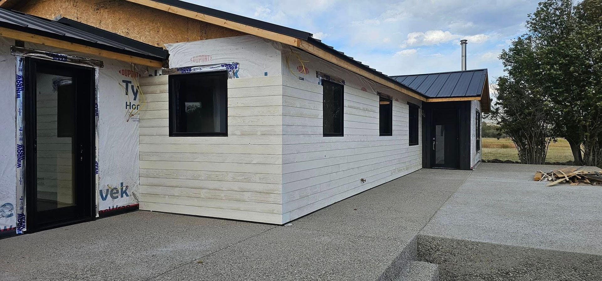 A single-story home under construction with white exterior sheathing, black window frames, and a dark metal roof.
