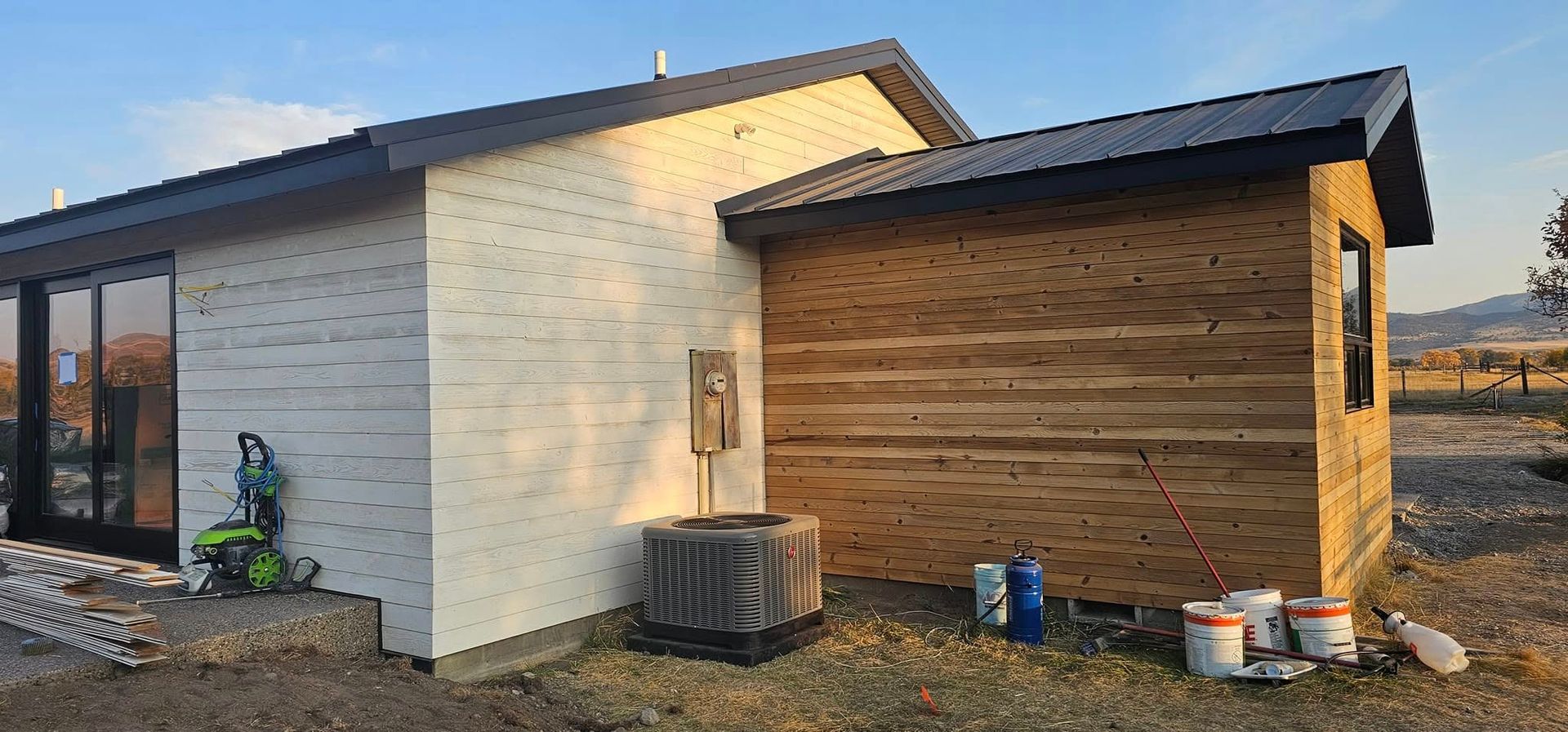 A house under construction with a white exterior wall next to a wood-paneled room and an air conditioning unit outside.