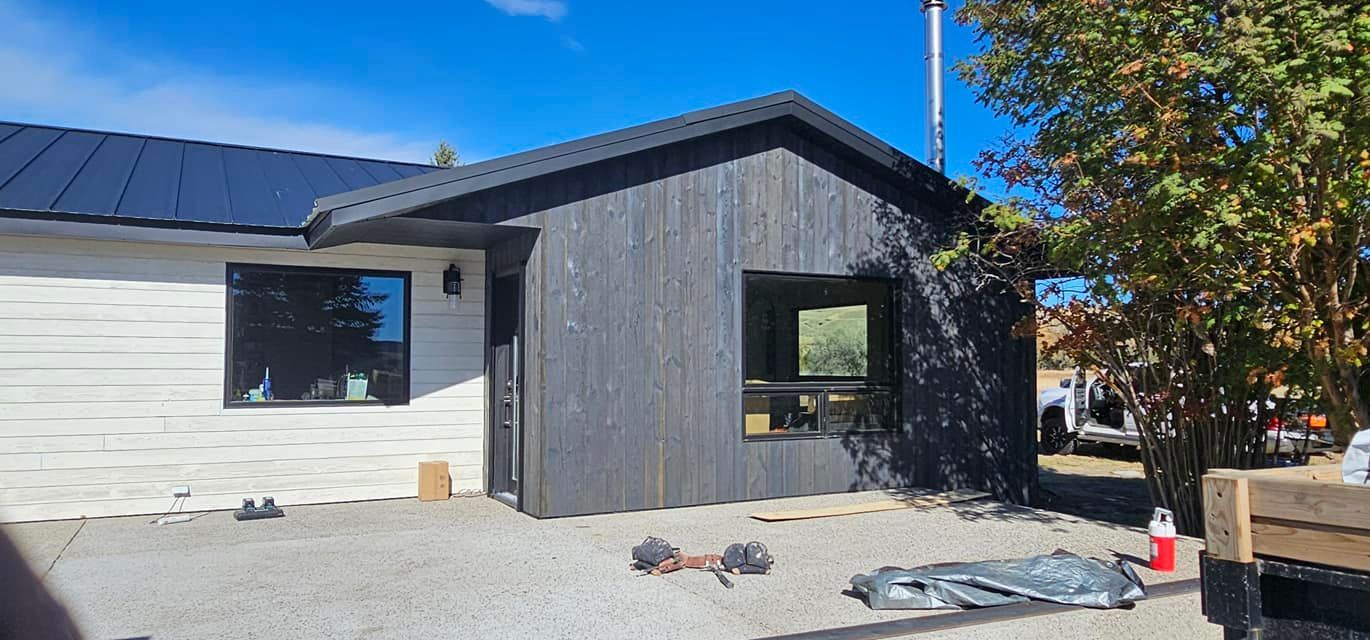 A house exterior with white horizontal siding and a dark, charcoal-colored vertical wood-paneled bump-out under a gable.