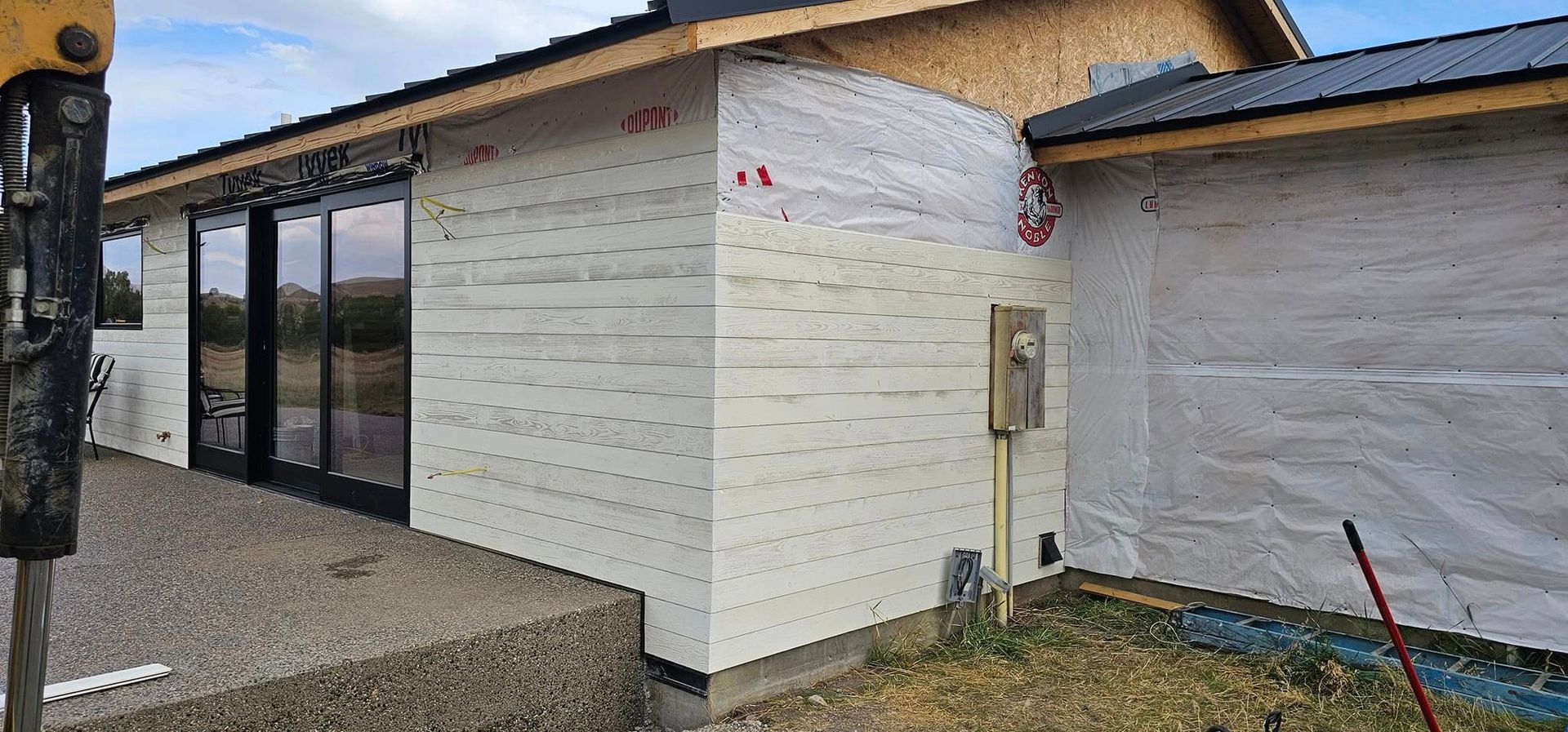 Exterior of a building under construction featuring white insulating panels and a partial metal roof, next to a gravel area.