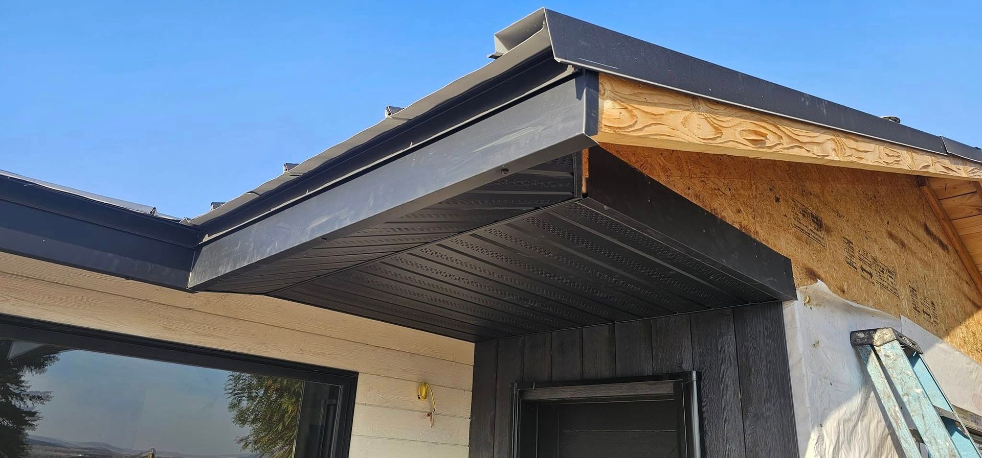 Black soffit and fascia installed on the exterior corner of a house under construction with exposed wood sheathing.