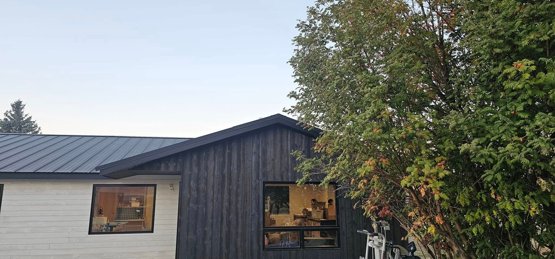 A house with light-colored horizontal siding on the left, dark vertical siding on the right, and a dark metal roof.