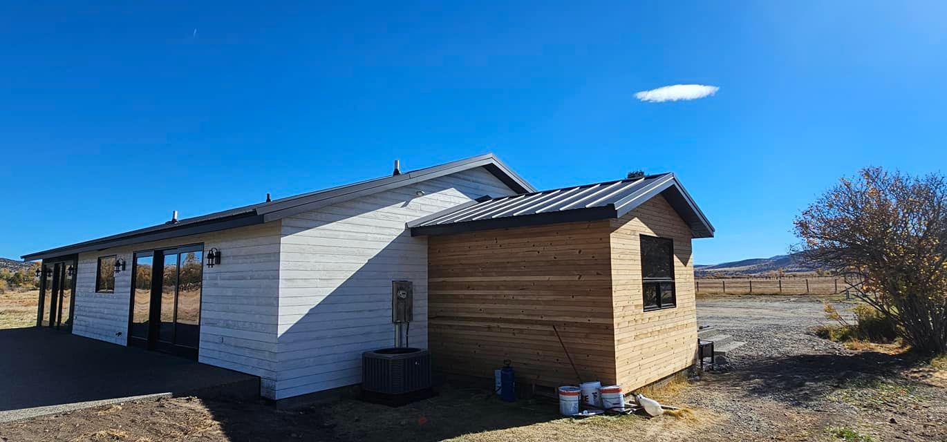 A single-story house with white siding and a brown wooden addition under a clear blue sky.