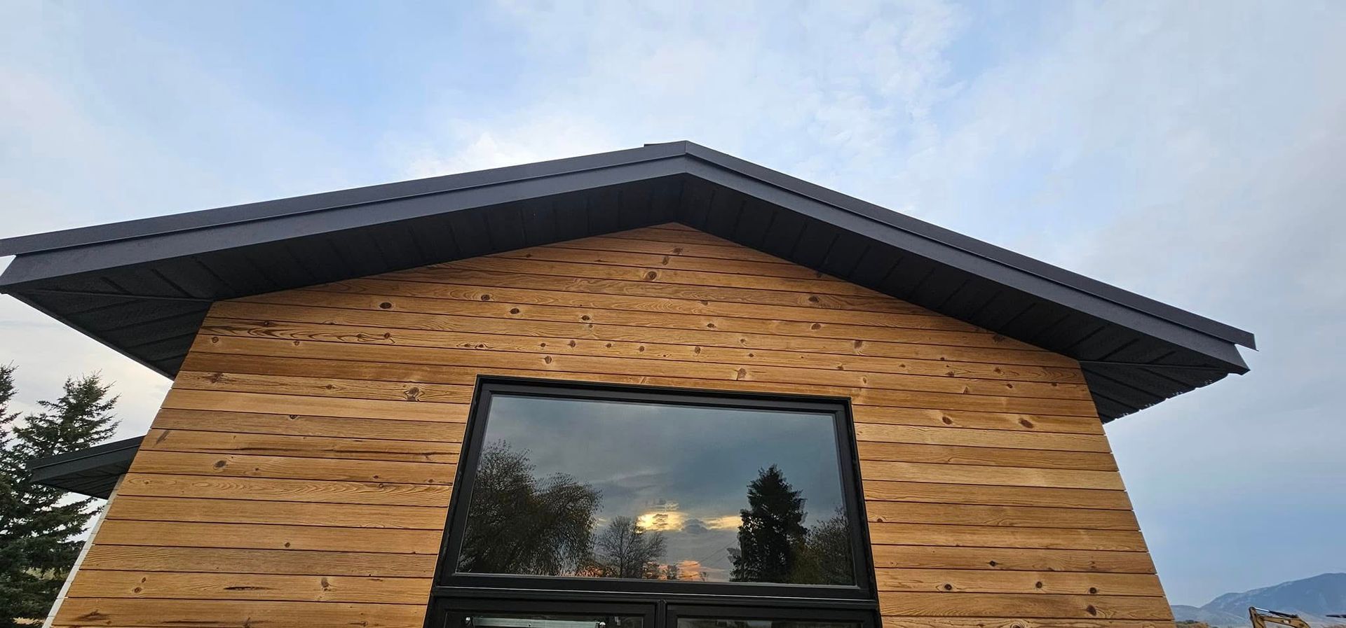 A low-angle view of a building exterior with textured, light brown wood siding and a large, dark-framed central window.