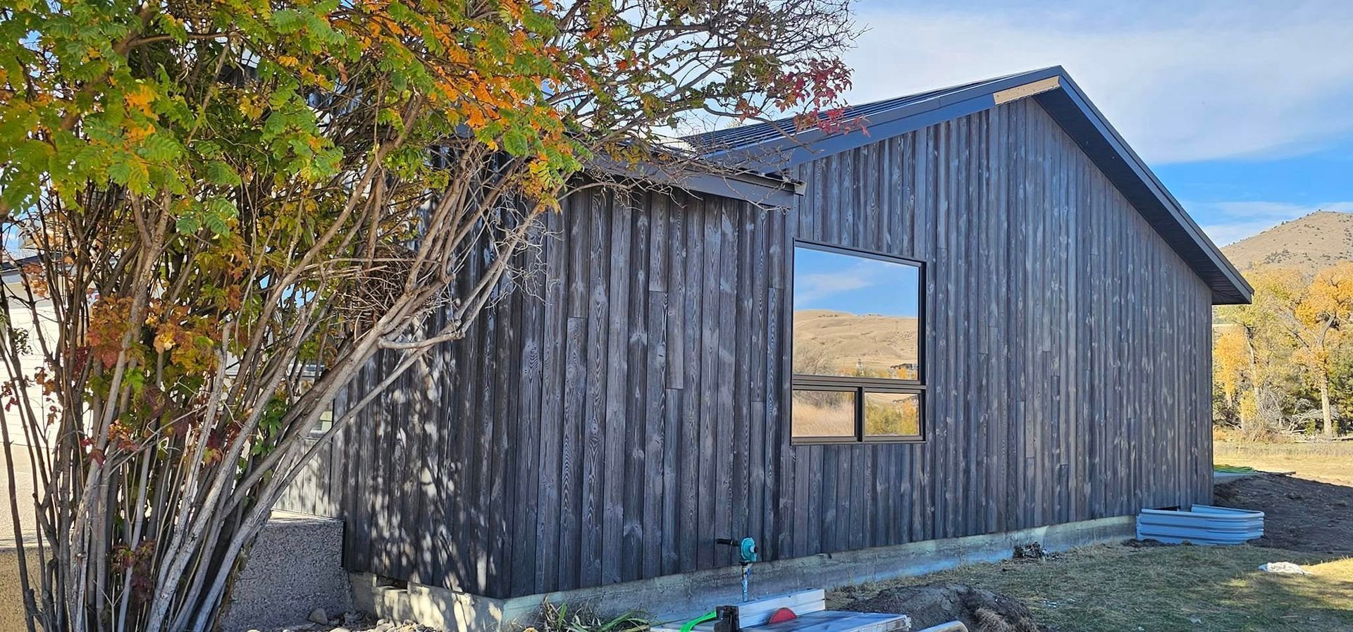 A modern single-story building with dark, vertically-oriented wooden siding and a rectangular window, set in a rural area.
