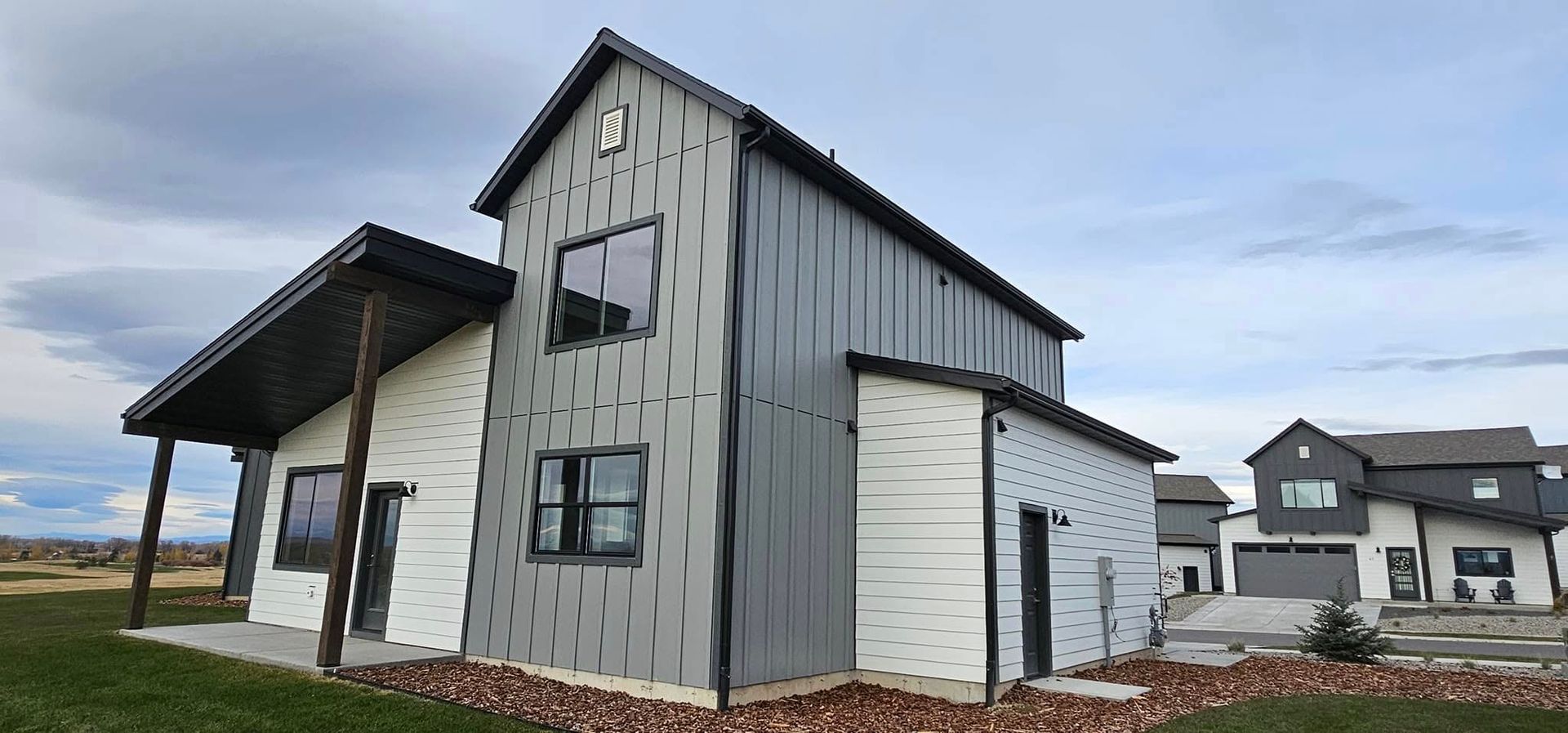 A modern two-story home with grey metal siding and white horizontal panels, set against a bright, cloudy sky.