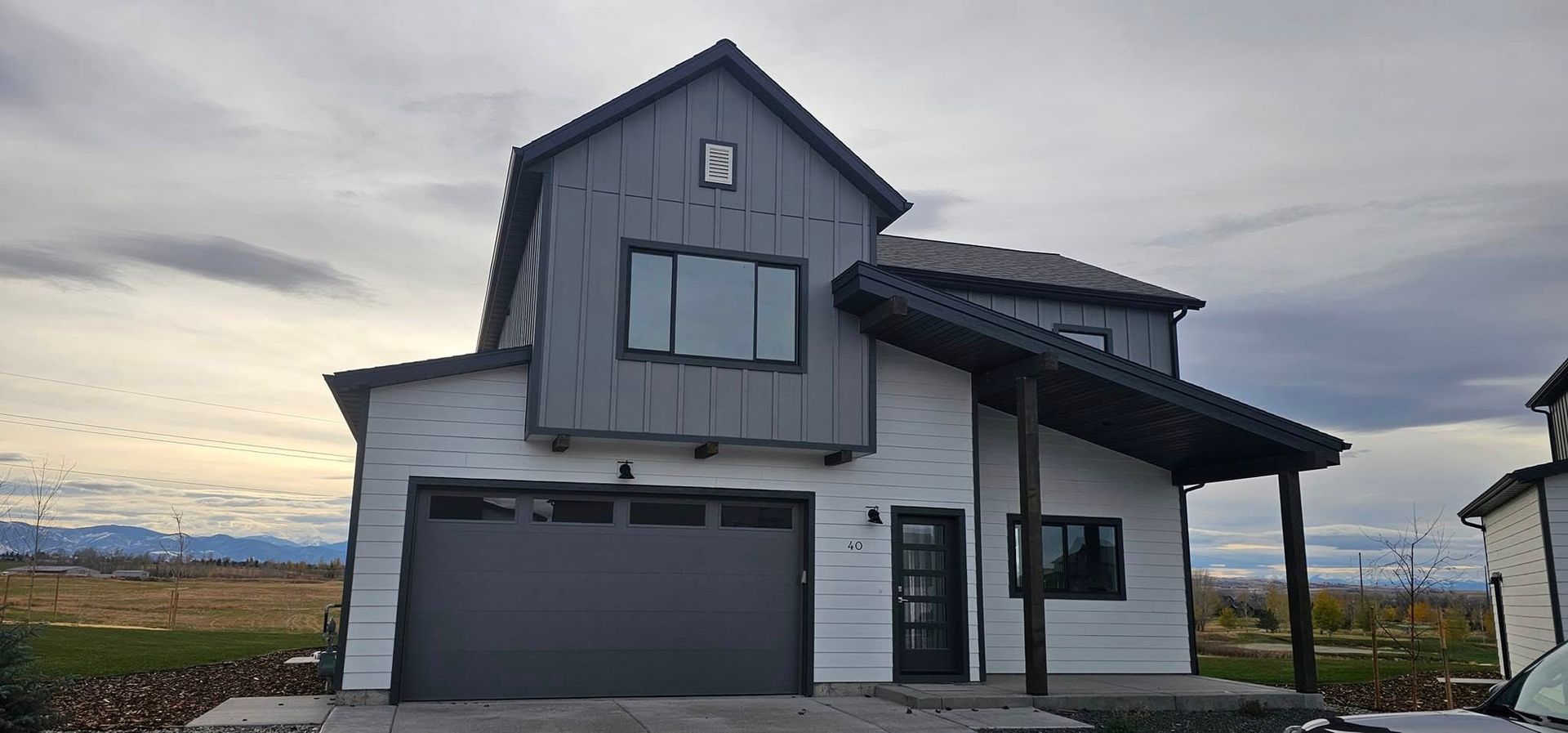 A two-story modern farmhouse with white horizontal siding, a gray board-and-batten upper gable, and a dark garage door.