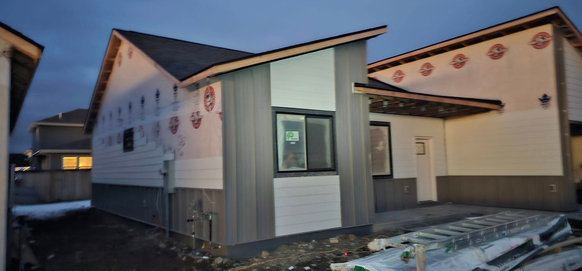 Exterior of a modern house under construction, featuring vertical grey siding and horizontal white panels at twilight.
