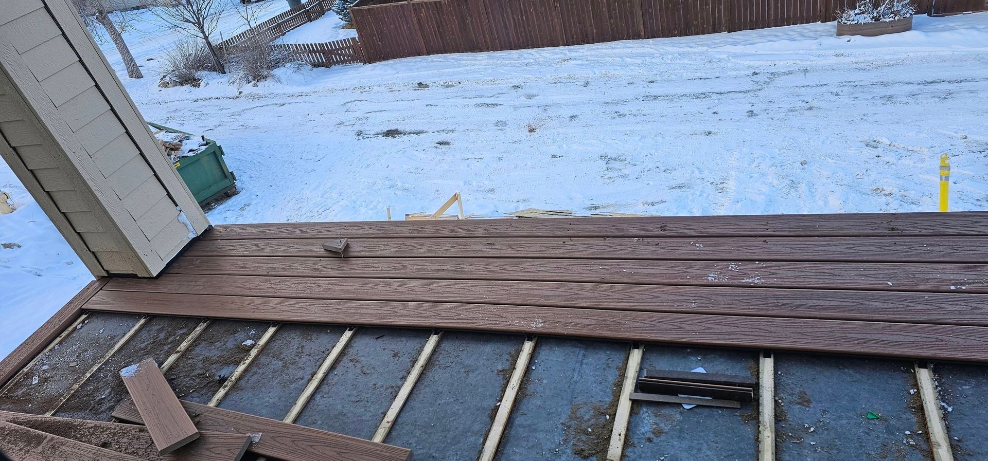 A partially demolished wooden deck with visible joists and snow-covered ground in the background.
