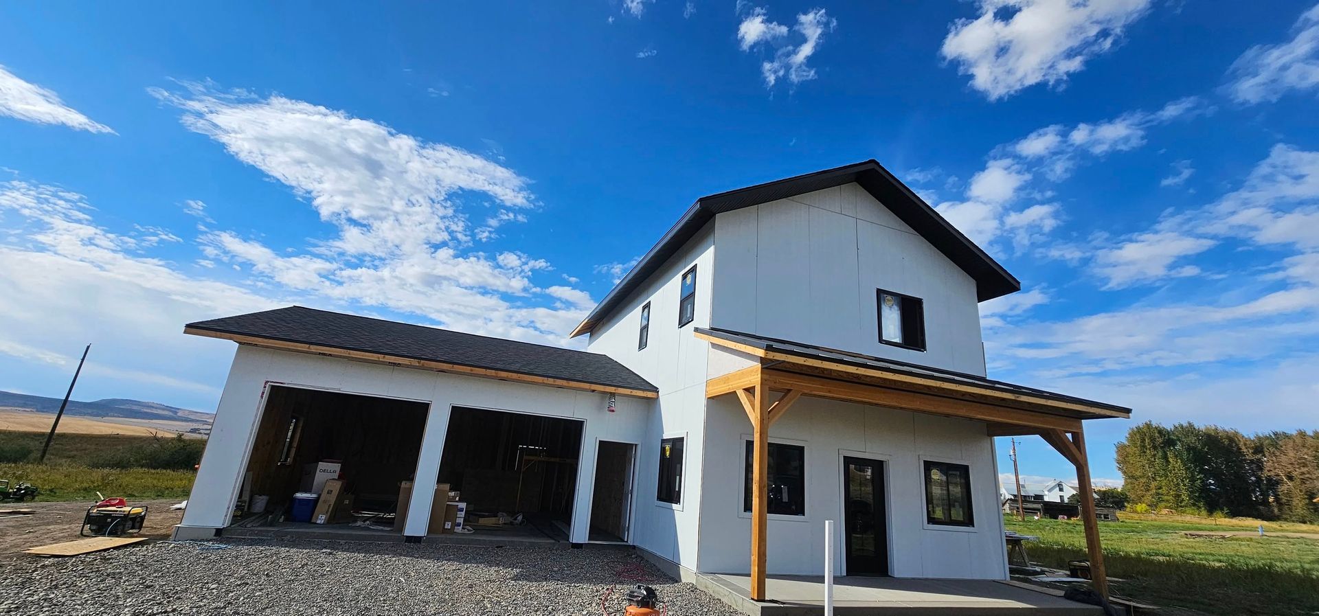 A two-story white house under construction with an attached garage and a wooden front porch against a blue sky.