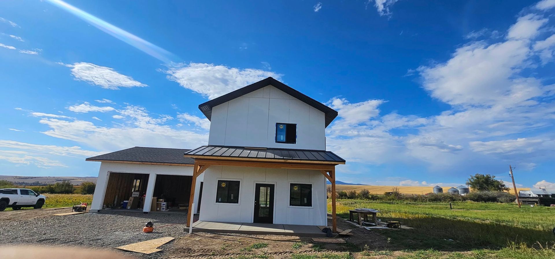 A two-story white house under construction with an attached garage under a bright blue sky with scattered clouds.