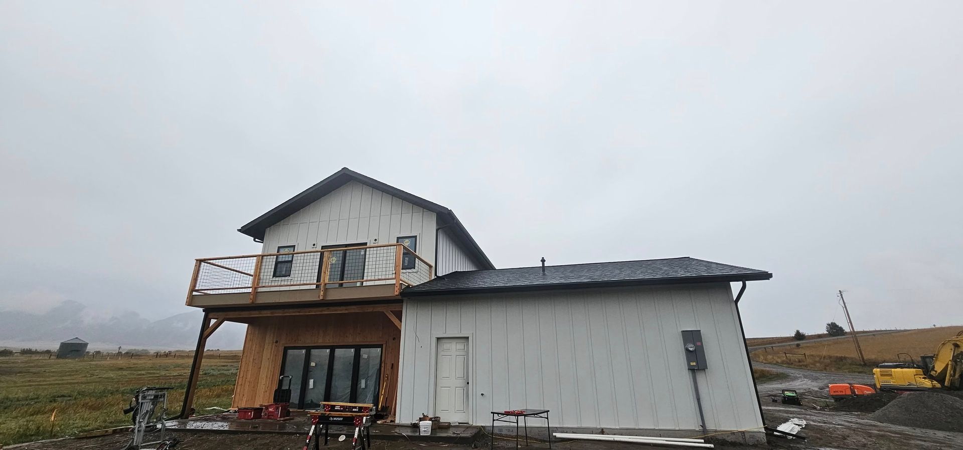 A two-story home under construction with white siding, a balcony on the upper level, and a flat-roofed garage, outdoors.