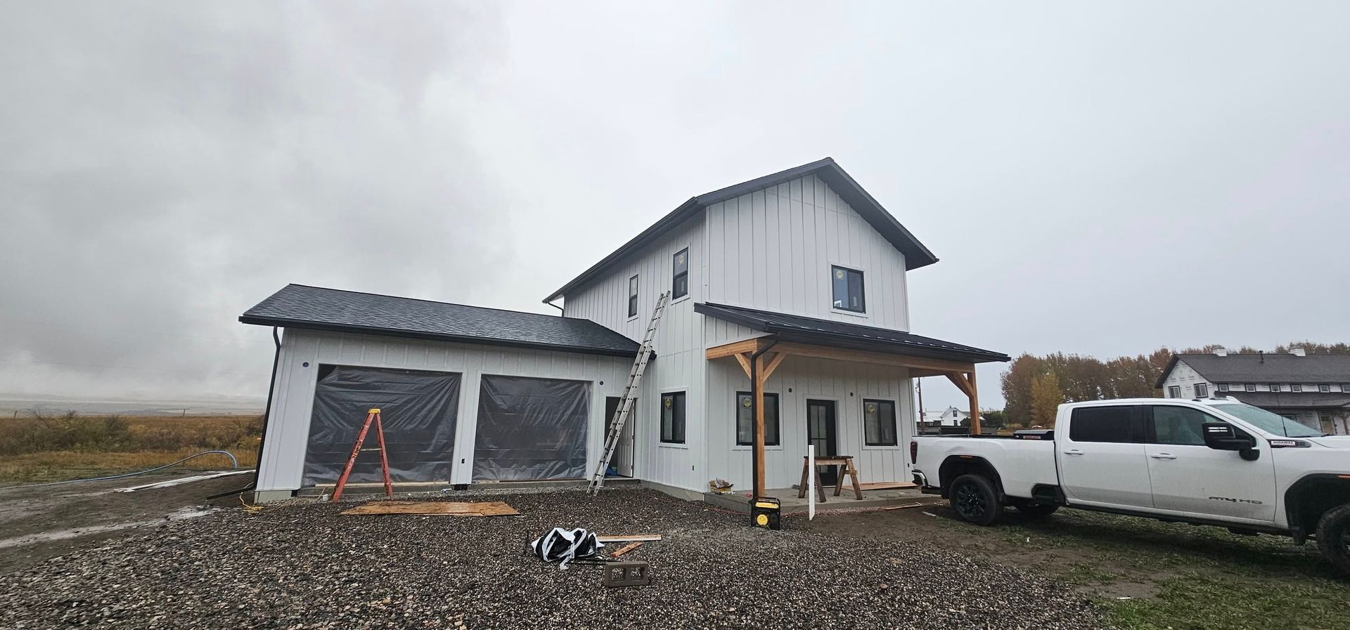 A two-story white house under construction with a garage, covered porch, and a white pickup truck parked in front.