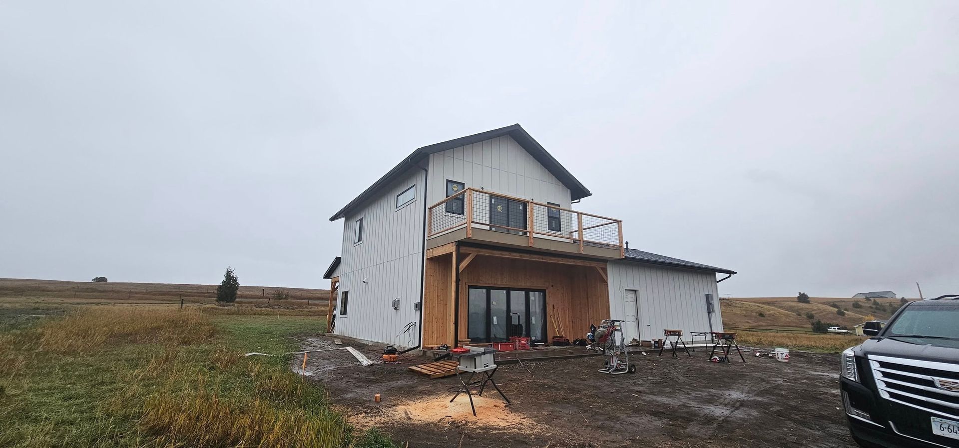 A two-story house under construction with white exterior siding and a wooden deck, set on an open, cloudy landscape.