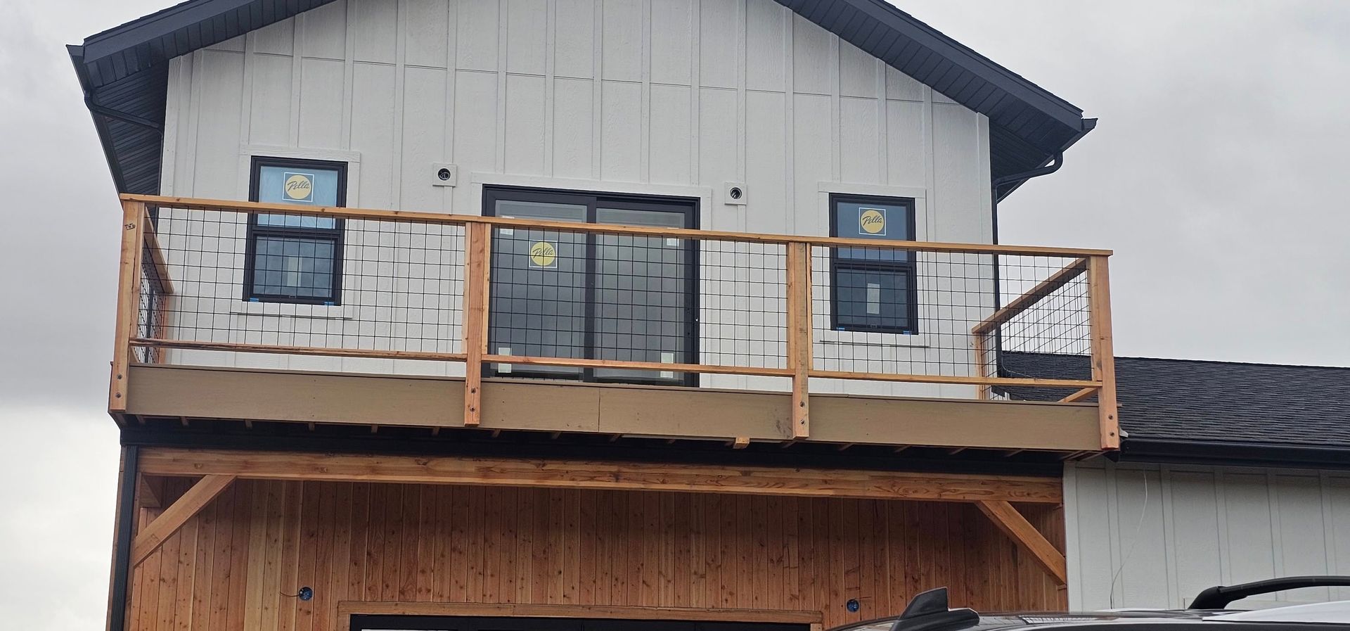 A partially finished house with a wooden deck, rustic railing, and white vertical siding under a dark roof.