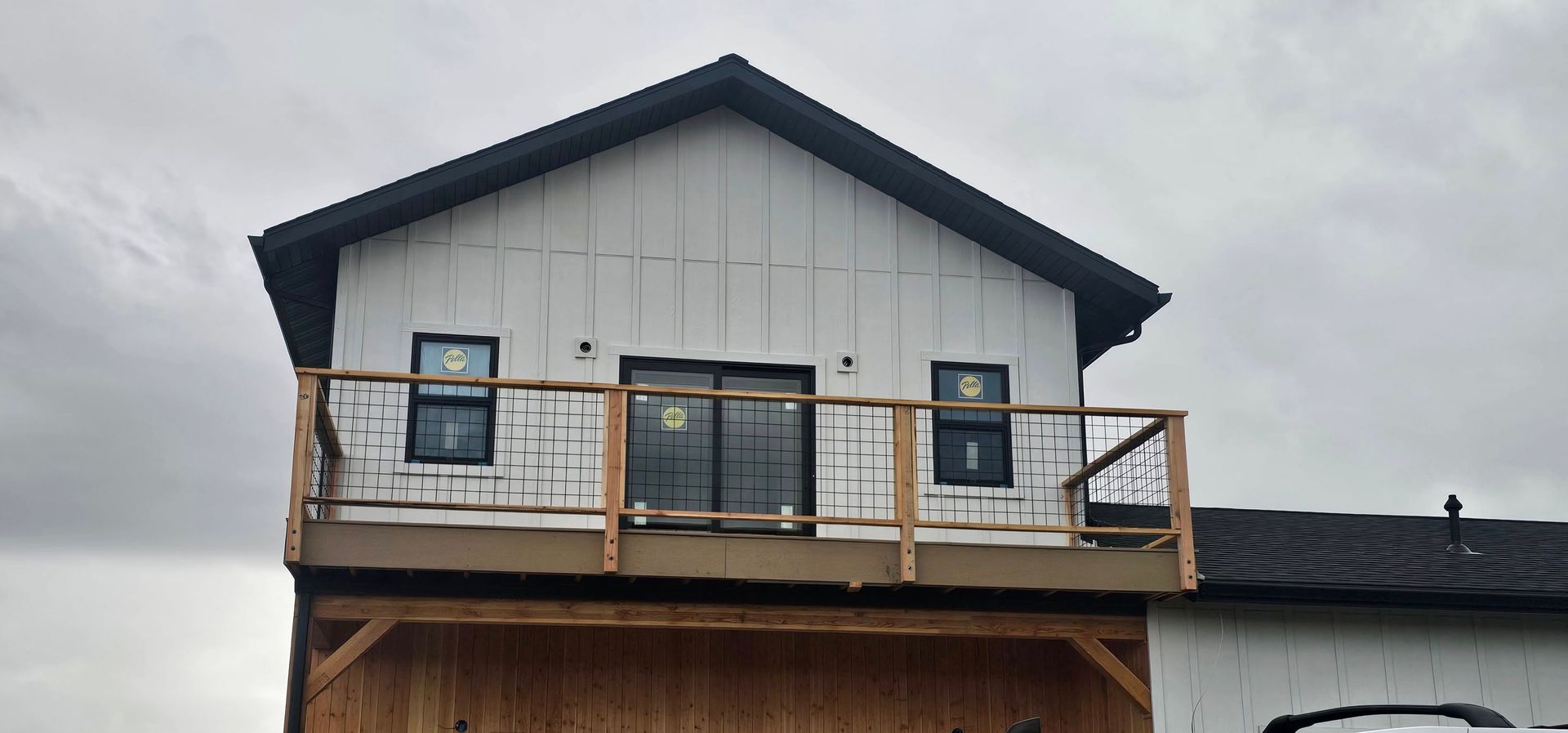 A two-story building under construction with a wooden balcony, white vertical siding, and dark window frames.
