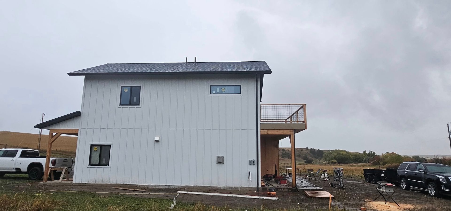 A two-story white house under construction with a dark roof and wooden porch, located in a rural, overcast setting.