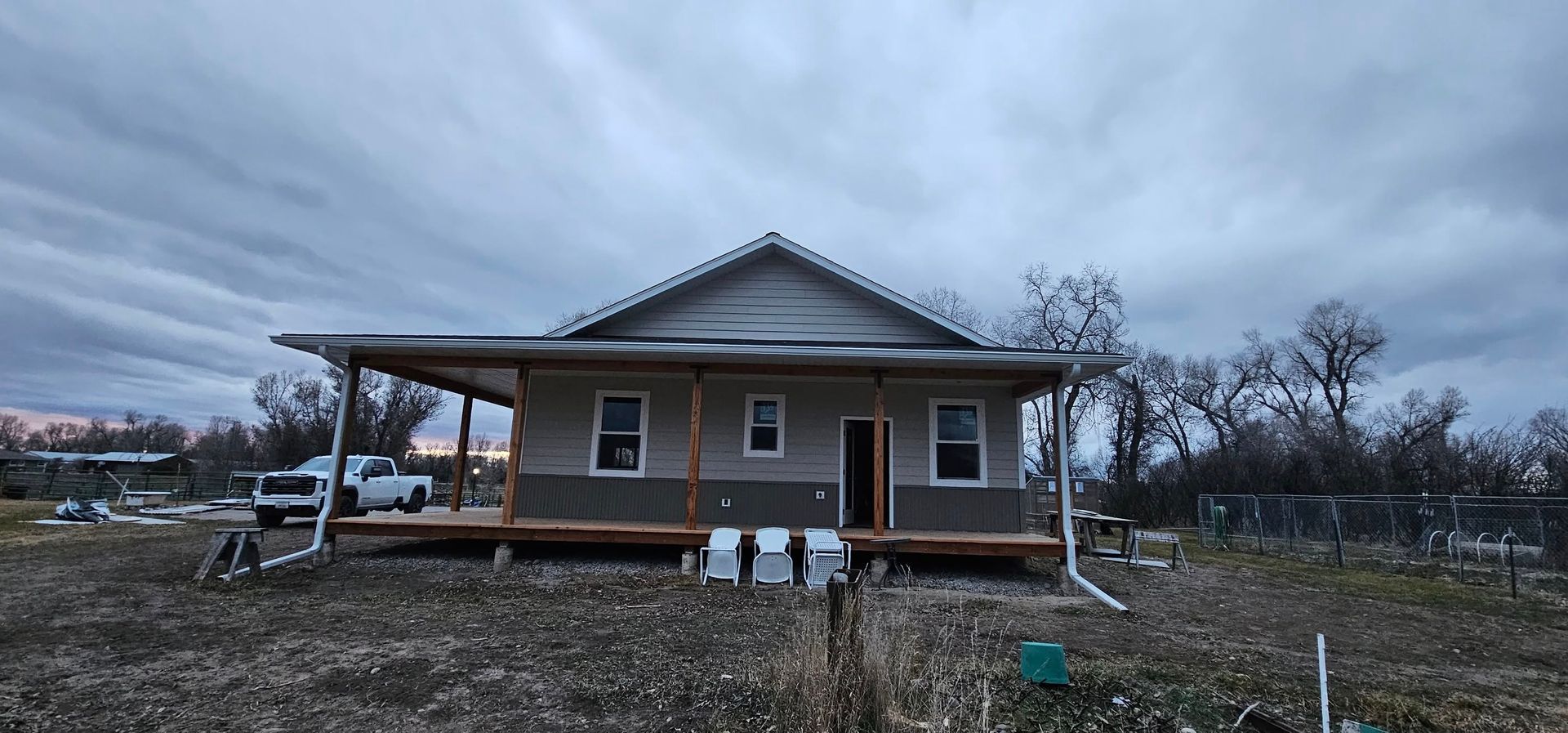 A single-story house with a wooden front porch, light siding, and a dark stone base, set on a lot under a cloudy sky.